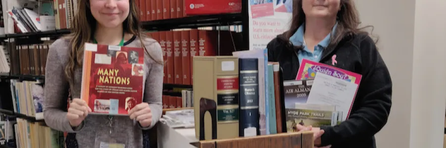 Two women in front of book shelves holding up government publications.