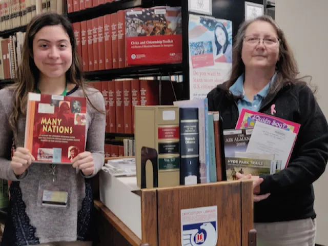 Two women in front of book shelves holding up government publications.